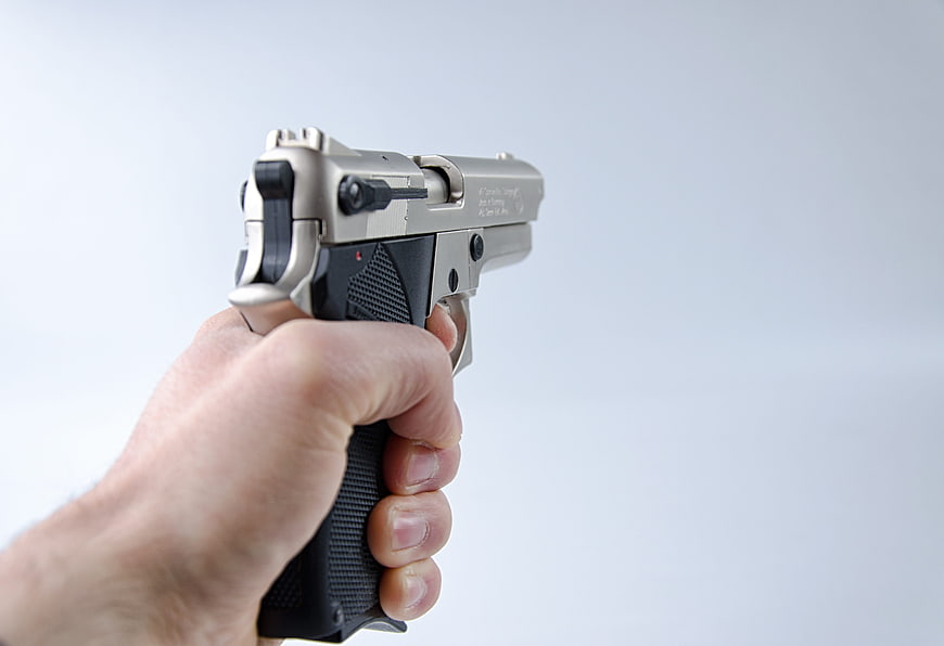 Hand Holding Silver Pistol Against White Background
