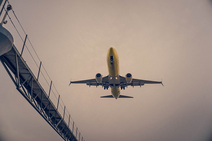 Yellow Airplane Landing Overhead with Bridge Structure