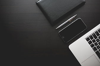 Minimalist dark workspace with laptop, smartphone, and notebook