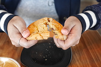 Hands Breaking Chocolate Chip Cookie Over Black Plate