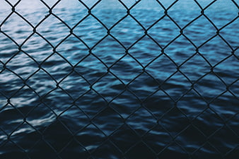 Chain link fence over blue ocean water background