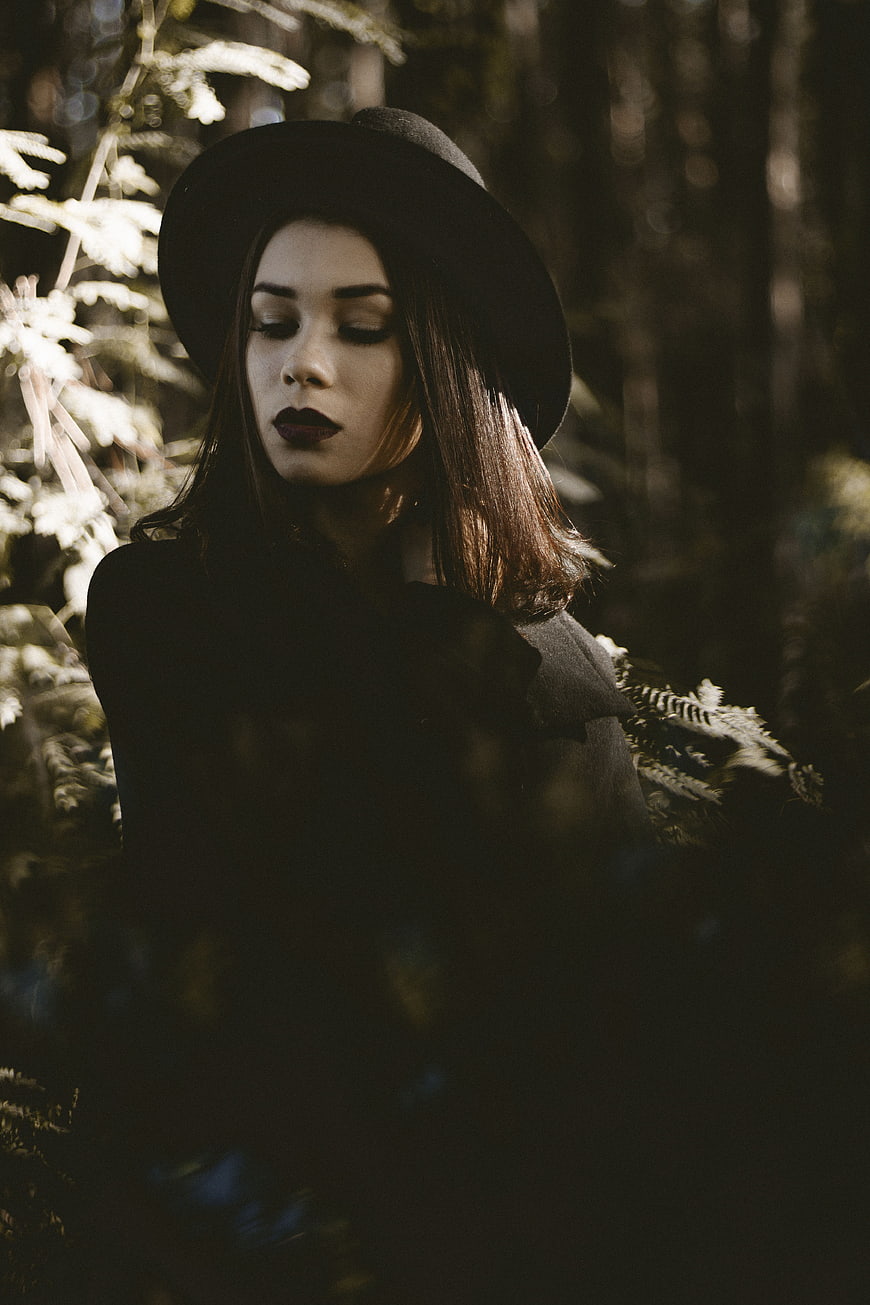 Mysterious woman in black hat standing in dark forest