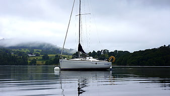 White sailboat moored on calm lake with misty mountains