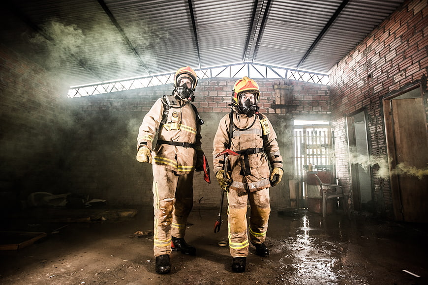 Two Firefighters in Full Gear Standing in Smoky Burnt Building