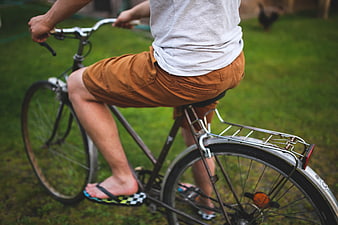 Man riding bicycle in shorts and flip-flops on grass