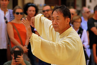 Asian man performing Tai Chi in a public square with onlookers