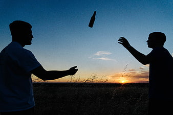 Silhouettes of two men tossing a bottle at sunset