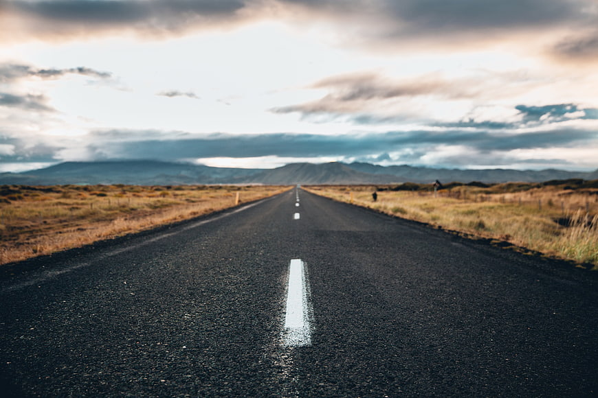 Empty asphalt road stretching to mountains under cloudy sky