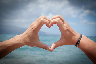 Hands forming heart shape against ocean background