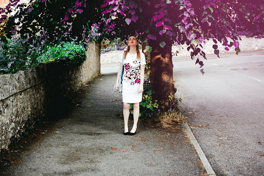 Woman in White Dress Standing Under Purple Tree on Sidewalk