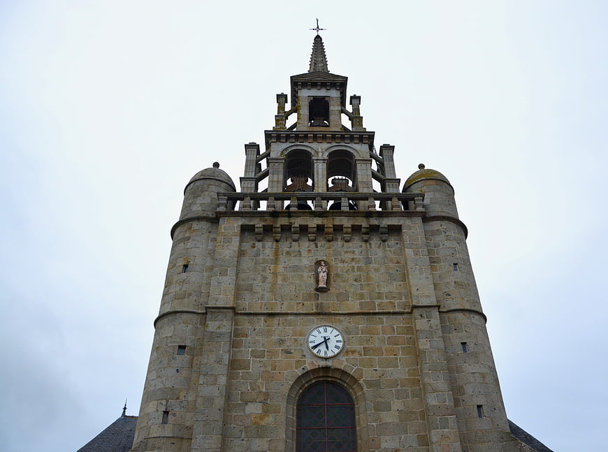Historic stone church bell tower with clock and bells against overcast sky