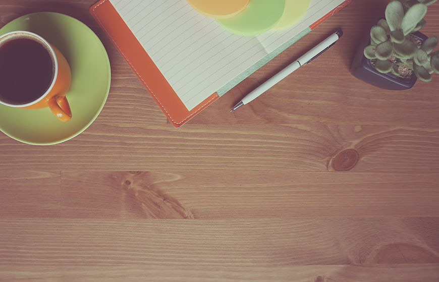 Flat Lay of Coffee Cup, Notebook, and Pen on Wooden Desk