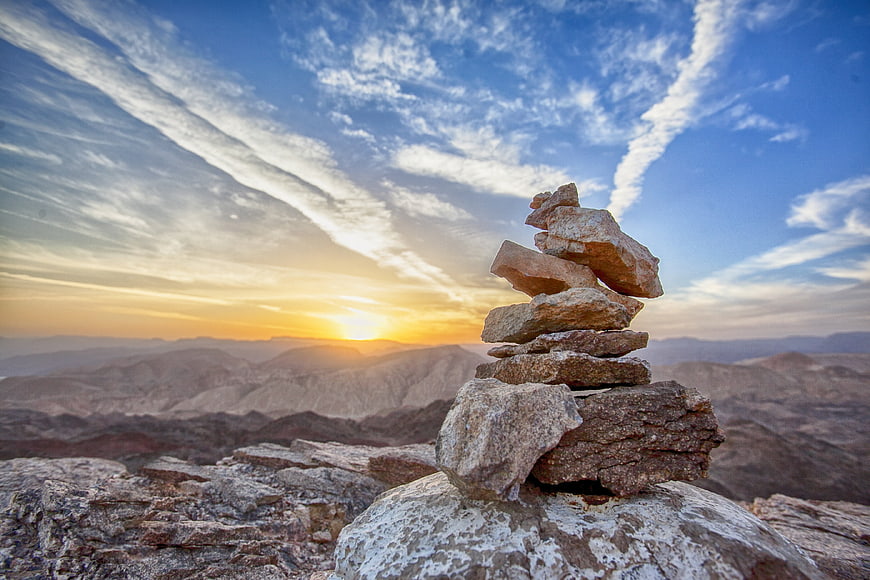 Balanced rock cairn on mountain peak at sunset