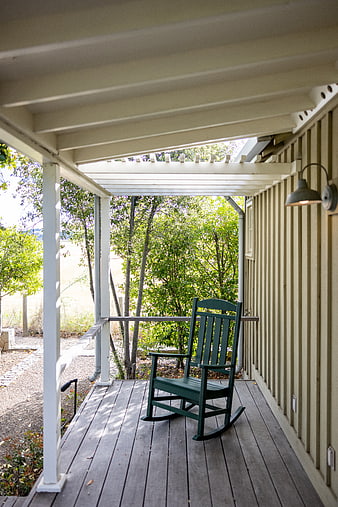 Green rocking chair on rustic wooden porch with trees