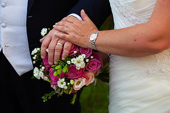 Close-up of wedding couple holding hands with bouquet and rings