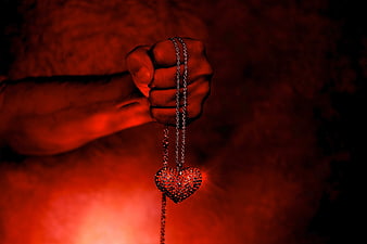 Hand holding sparkling heart pendant against red background