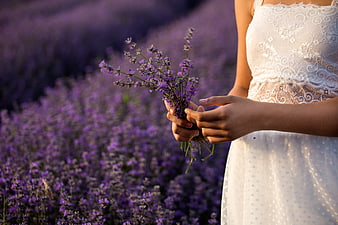 Woman in white lace dress holding lavender bouquet in purple field
