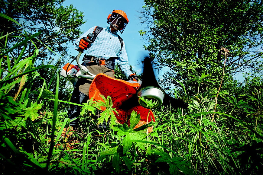 Gardener using a string trimmer in tall grass