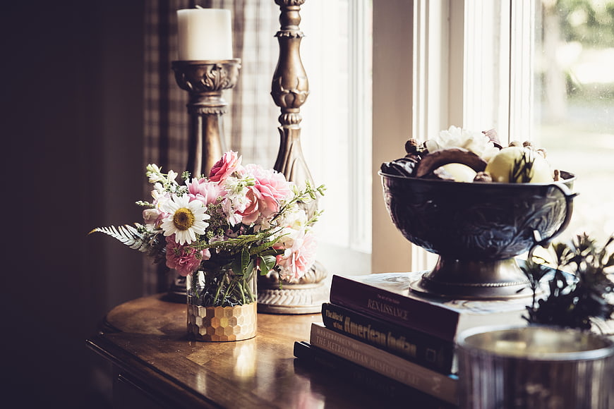 Rustic floral arrangement and books on wooden table by window