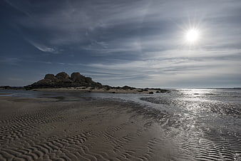 Sandy Beach with Ripples and Rocky Outcrop Under Bright Sun