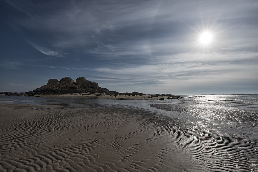 Sandy Beach with Ripples and Rocky Outcrop Under Bright Sun