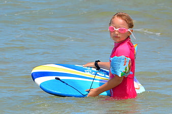 Young girl with surfboard and goggles in ocean water