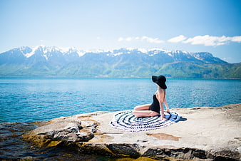 Woman in swimsuit relaxing on rocky lake shore with mountains