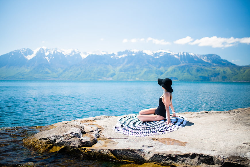 Woman in swimsuit relaxing on rocky lake shore with mountains