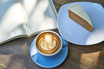 Latte with heart art, cake slice, and open book on wooden table
