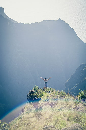 Man Standing on Cliff with Arms Raised in Victory
