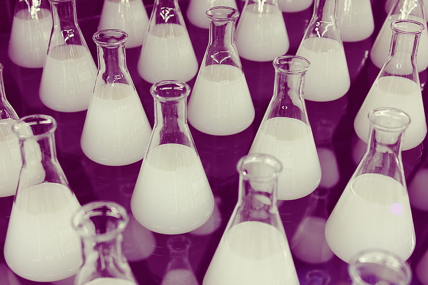 Erlenmeyer flasks with white liquid in purple laboratory setting