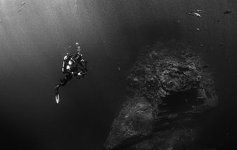 Scuba diver exploring underwater rock formation in black and white