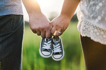 Couple Holding Baby Shoes in Field