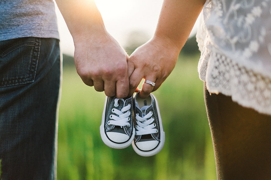 Couple Holding Baby Shoes in Field