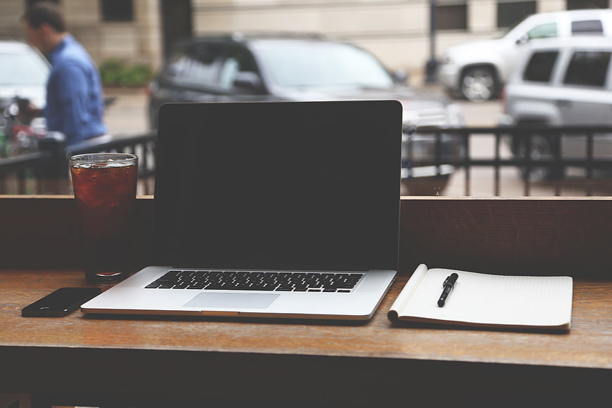 Laptop, notebook, and iced coffee on outdoor cafe table