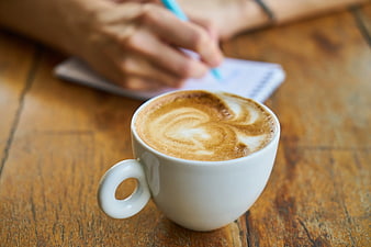 Latte Art Coffee Cup on Wooden Table with Writing Hand