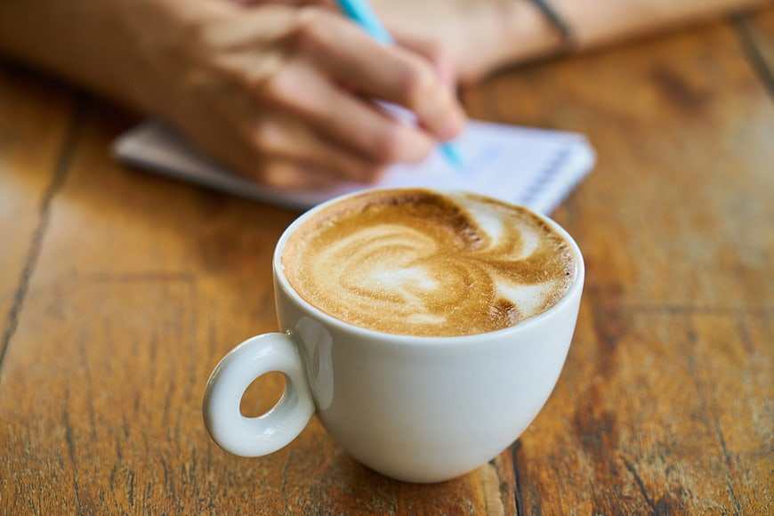 Latte Art Coffee Cup on Wooden Table with Writing Hand