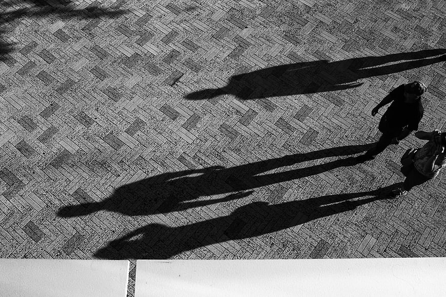 High angle black and white photo of people walking on herringbone pavement