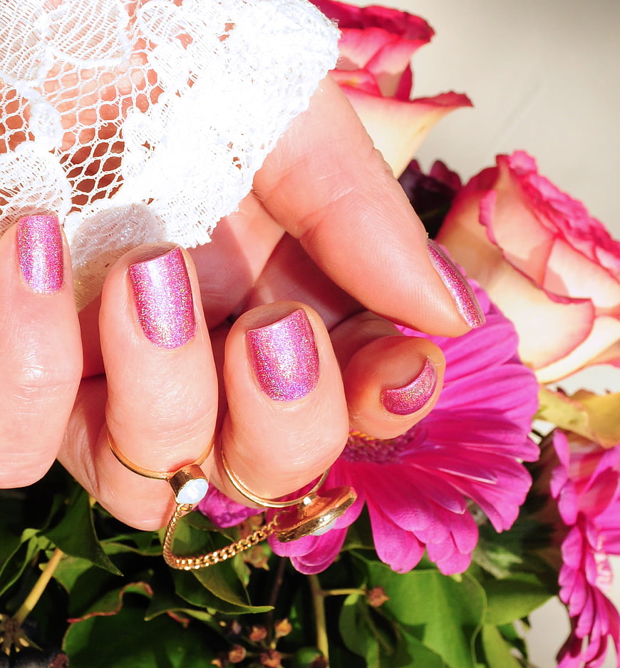 Close-up of hand with pink glitter manicure holding flowers