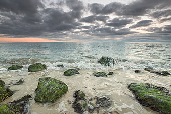 Dramatic cloudy sunset over ocean waves crashing on mossy rocks