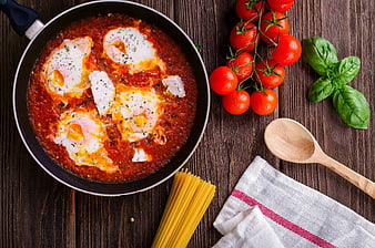 Shakshuka with eggs in tomato sauce on wooden table