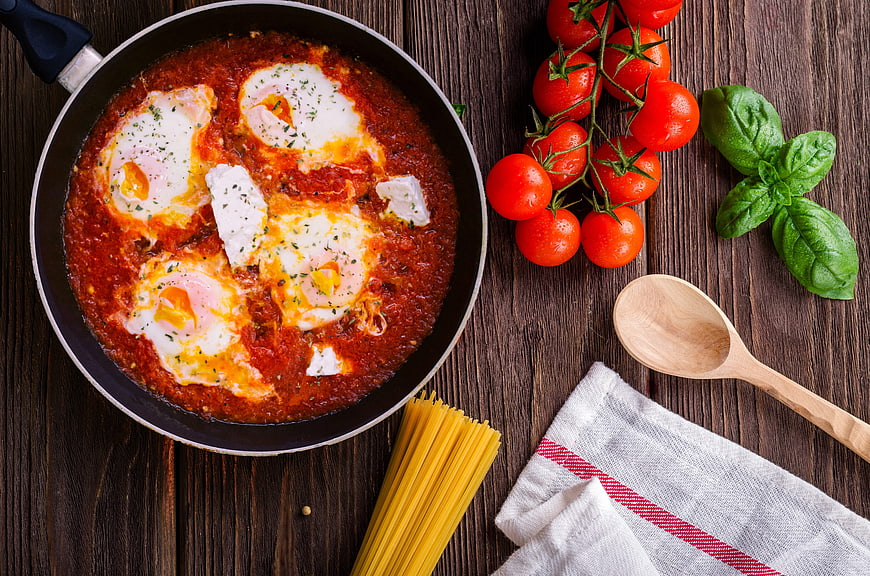 Shakshuka with eggs in tomato sauce on wooden table