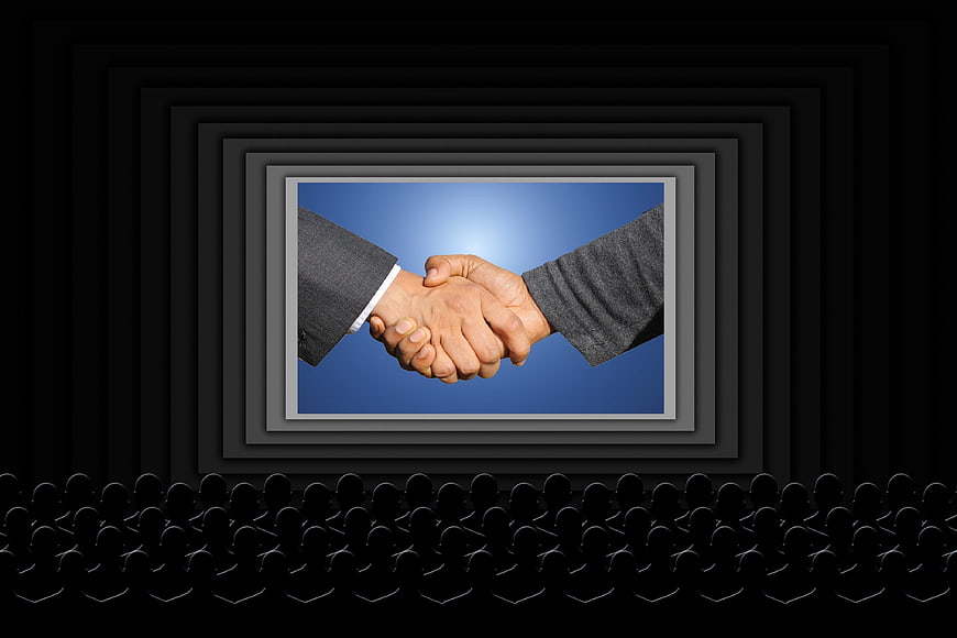 Business Handshake On Movie Screen With Silhouetted Audience