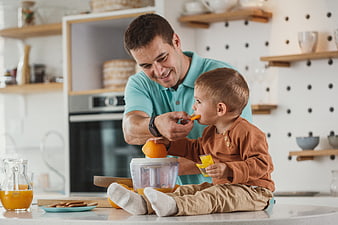 Father feeding son orange slice in bright modern kitchen