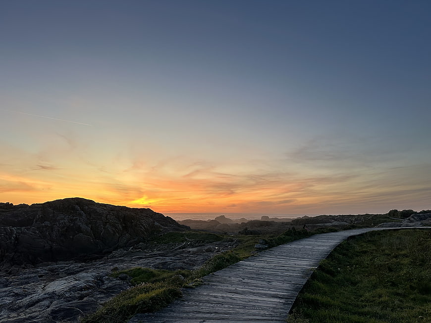Wooden boardwalk path leading to rocky coastline at sunset