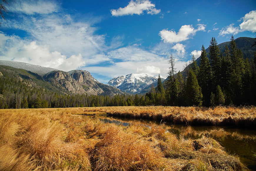 Golden autumn meadow with stream and snow-capped mountains
