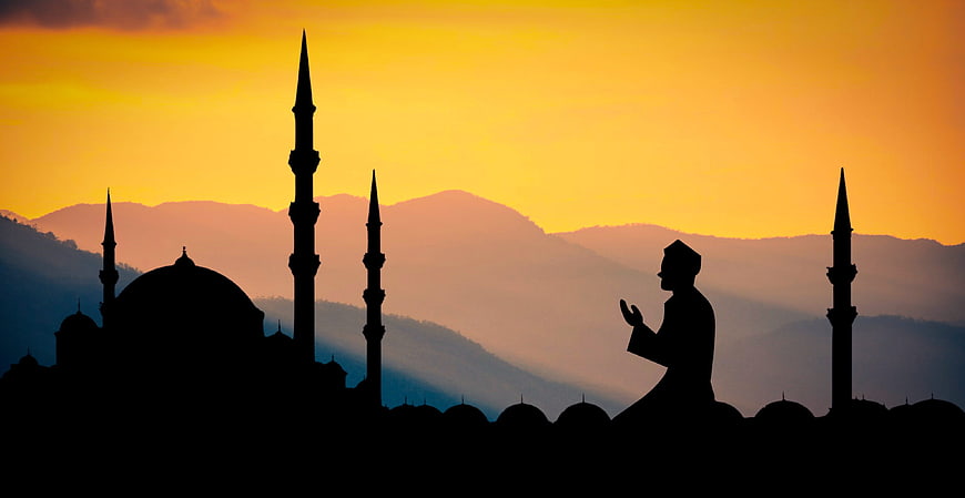 Silhouette of Muslim man praying at mosque during sunset