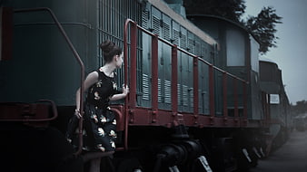 Elegant woman in floral dress posing by vintage green train carriage