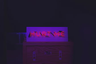 Red neon sign reading HURT ME on wooden crate