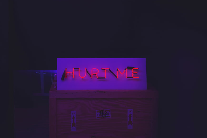 Red neon sign reading HURT ME on wooden crate